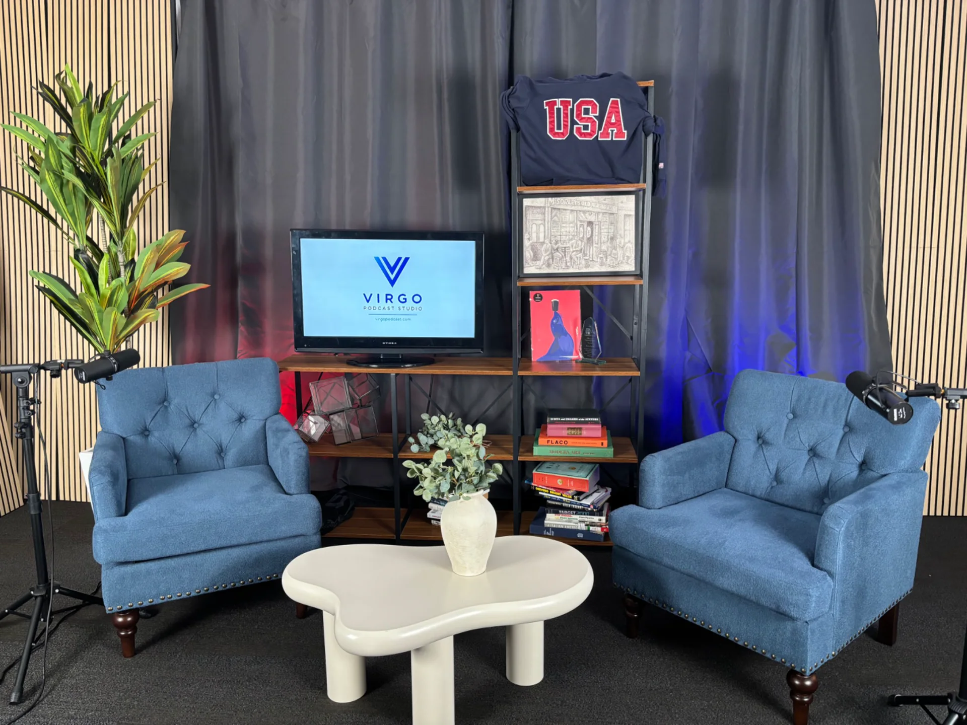 The updated VIRGO Podcast Studio set with two blue chairs, microphones, wood slat walls and a central screen